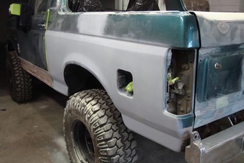 1996 Ford Bronco - Photograph of a lifted Bronco rear quarter in primer during paint prep, not a technical document.