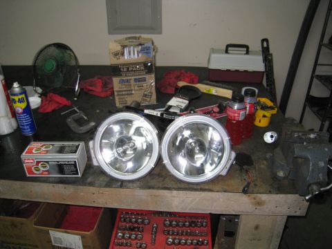 1996 Ford Bronco - A workbench is cluttered with various items including two large spotlights, a can of WD-40, a box of caulk, a fan, and a toolbox.