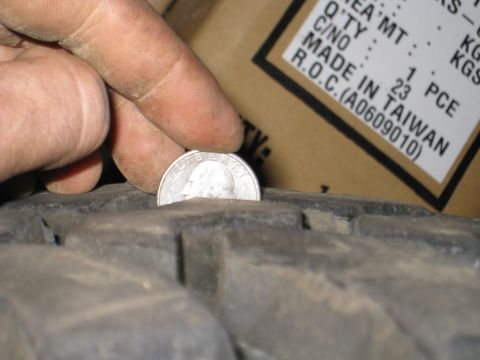 1996 Ford Bronco - A hand holds a quarter coin against the tread of a tire, indicating tread depth. A shipping label with text including "MADE IN TAIWAN" is v…