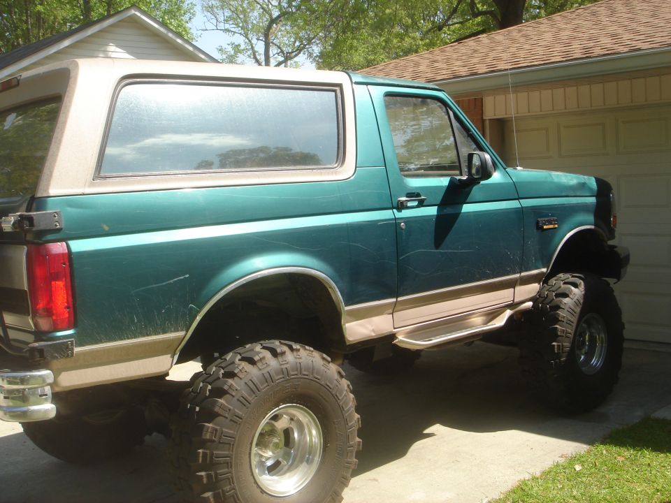 1996 Ford Bronco, lifted, teal with tan trim, large off-road tires, parked in driveway.