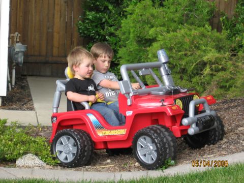 1994 Ford Bronco - Two children sit in a red toy fire rescue jeep parked outdoors.