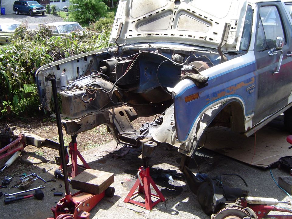 Disassembled 1979 Ford Bronco chassis and engine bay on jack stands outdoors.