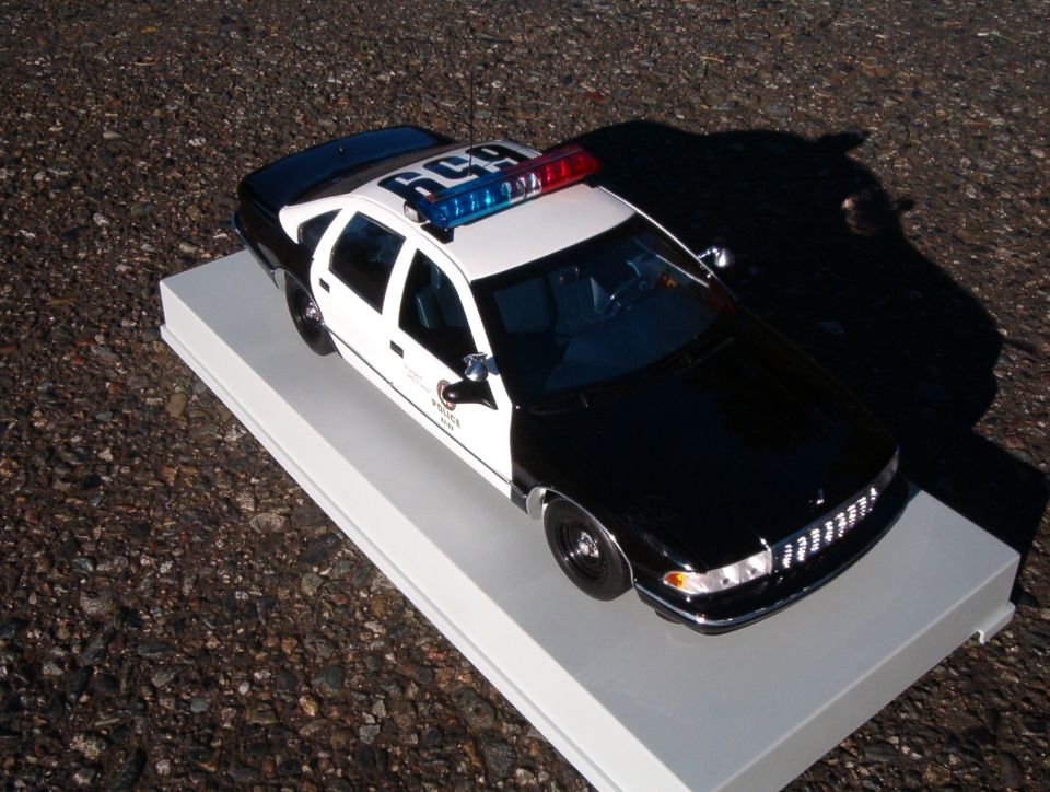 Black and white police sedan scale model on white display base, high-angle 3/4 front view
