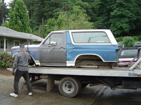 1979 Ford Bronco - A blue and grey Ford Bronco is loaded onto a flatbed tow truck, with 'Flowmaster' visible on the rear window.