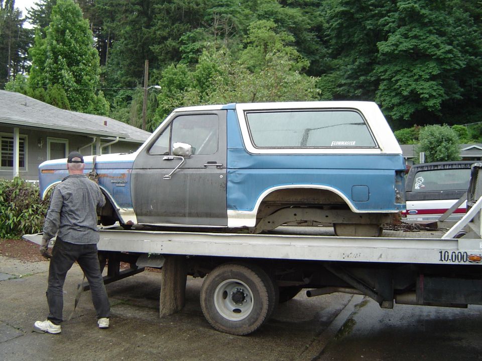 Side view of a blue and grey Ford Bronco on a flatbed tow truck. Text on rear window reads 'Flowmaster'