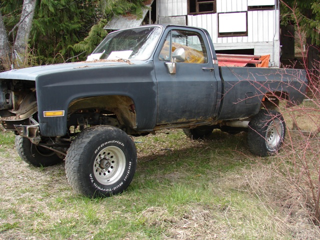 Lifted dark gray pickup truck with missing front end, parked on grass. BFGoodrich tires visible