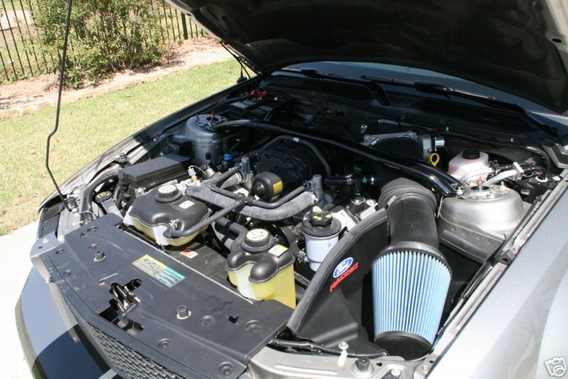 Engine bay with black cold air intake and blue conical filter, hood open, outdoors