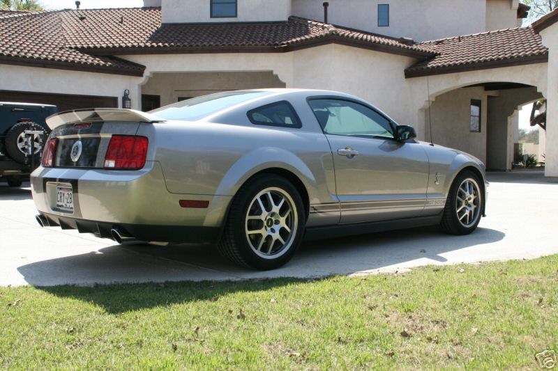 Silver Mustang Shelby GT500 coupe with stripes, rear 3/4 view in driveway