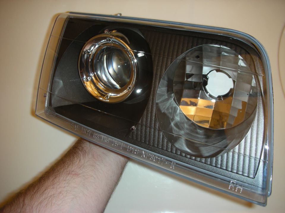 Hand holding a black projector headlight assembly with clear lens