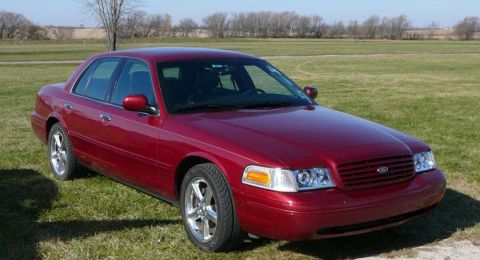 1998 Ford Crown Victoria - Front three-quarter view of a dark red Ford full-size sedan with chrome wheels parked in a grassy field.