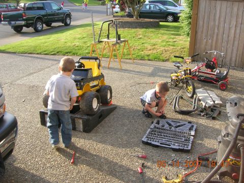 1996 Ford Bronco - Two young boys are engaged with toy vehicles and tools in a driveway, with a green pickup truck in the background.