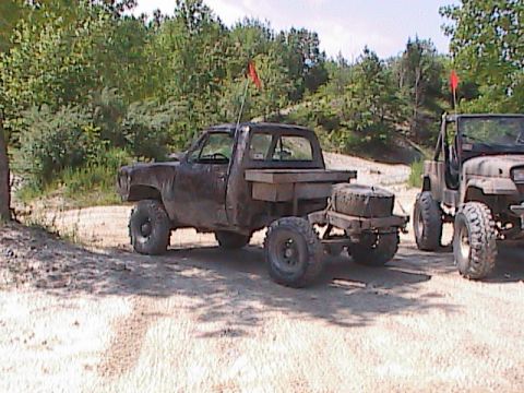1980 Dodge Magnum - Two off-road vehicles, a pickup truck and a Jeep, are parked on a dirt lot with trees in the background.