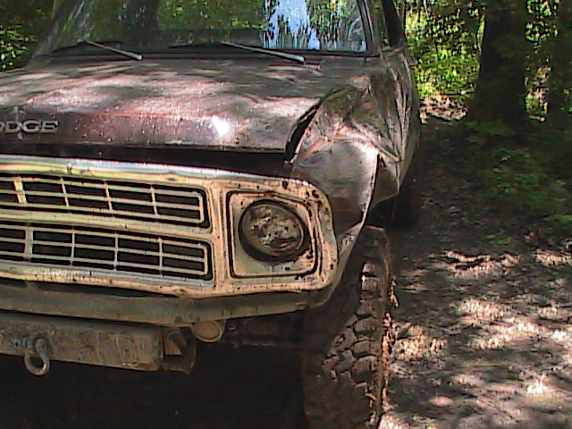 Front view of a damaged Dodge pickup truck with a dented fender and grille. Off-road tires are visible