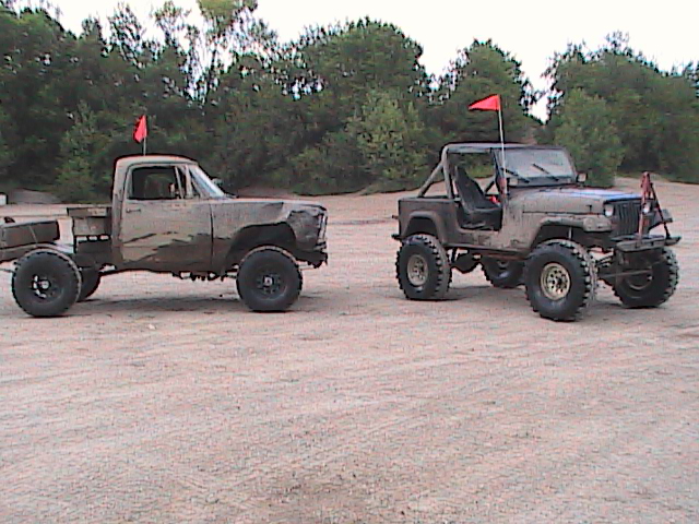 Muddy pickup truck and Jeep parked on dirt, both with red flags