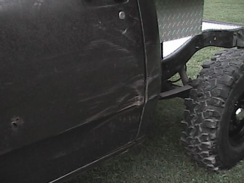 1980 Dodge Magnum - Close-up view of a damaged black pickup truck's rear quarter panel and a off-road tire.