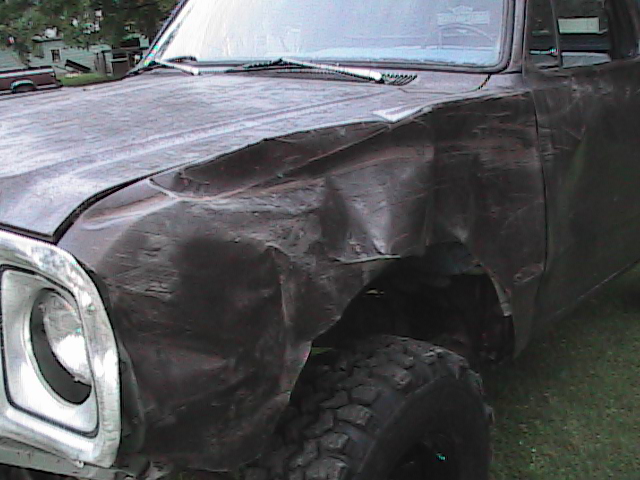 Damaged dark colored truck fender and hood with chrome headlight bezel. Off-road tire visible