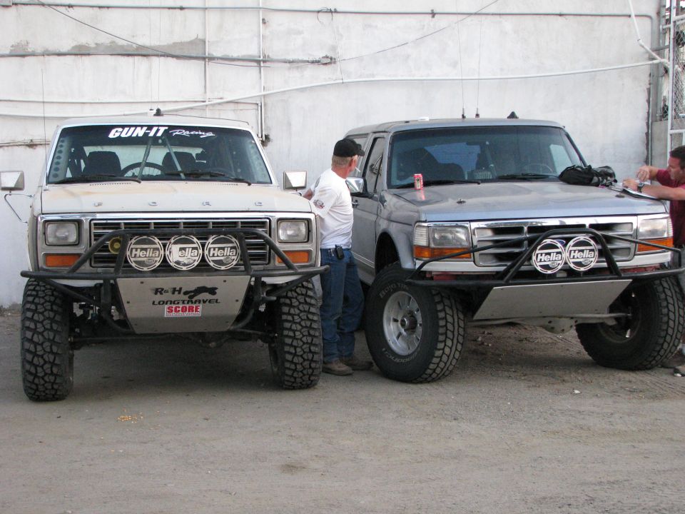 White and silver off-road Ford trucks with tube bumpers and Hella lights parked in dirt lot