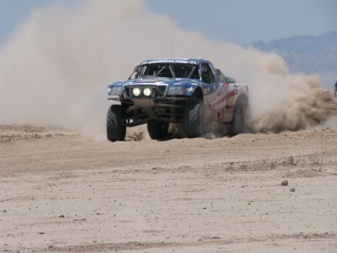 2008 Ford Bronco - A custom off-road truck races through the desert, kicking up a large cloud of dust.