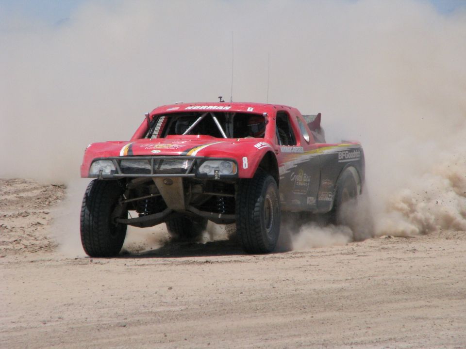 Red off-road racing truck kicking up dust on a dirt track. Number 8 is visible on the door