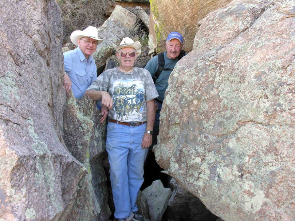 Three men standing among large rocks outdoors