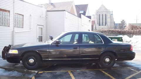 2000 Ford Crown Victoria - A black 2000 Ford Crown Victoria sedan is parked in a lot with a building and church in the background.