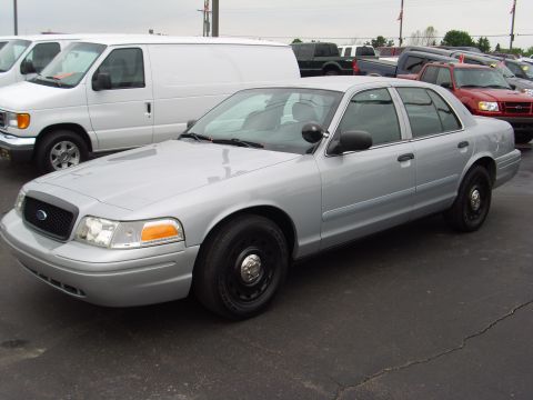2004 Ford Crown Victoria - Silver 2004 Ford Crown Victoria police car seen from the front-right side, parked in a lot.