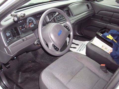 2004 Ford Crown Victoria - The interior of a police car shows the dashboard, steering wheel, and passenger seat with a floor mat.