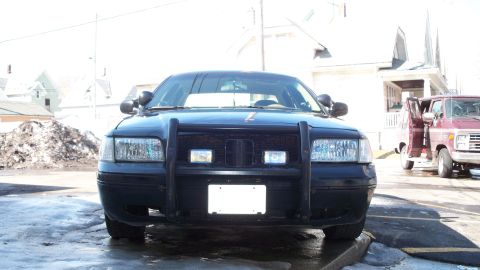 2000 Ford Crown Victoria - Black 2000 Ford Crown Victoria police car shown from the front, with a maroon van visible to the right.