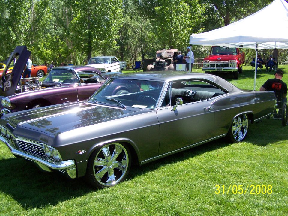 1965 Chevrolet Impala with custom wheels parked on grass, other cars and tents in background