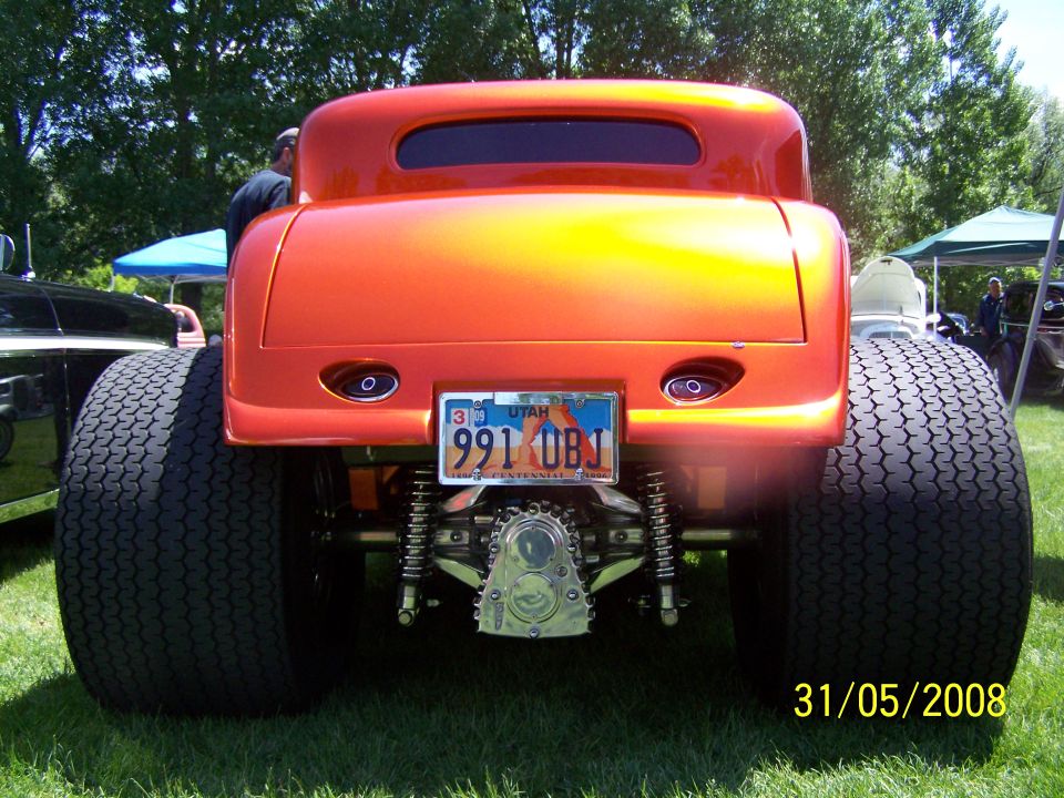 Rear view of an orange hot rod coupe with large rear tires and a license plate