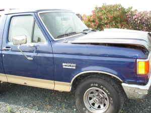 1991 Ford Bronco - This blue Ford Bronco shows damage to its hood and some wear on the lower body panels.