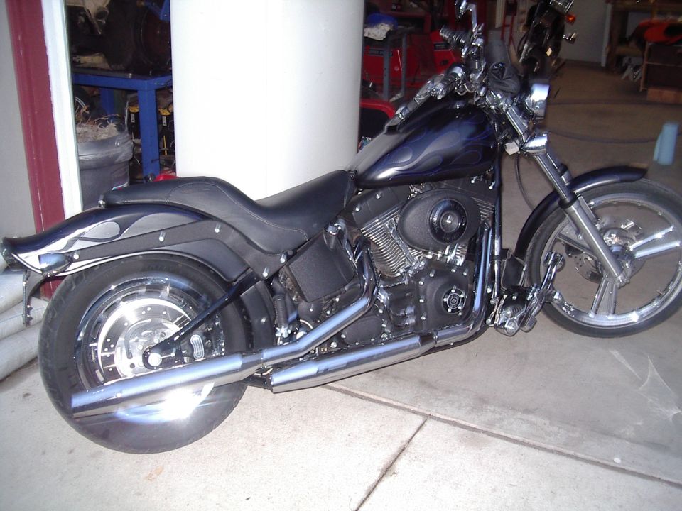 Black Harley Softail with blue flame tank graphics, side view in a garage