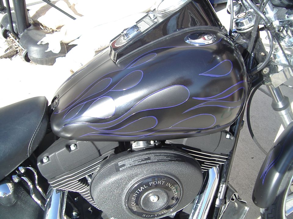 Black motorcycle fuel tank with purple flames, close-up on engine with 'Sequential Port Injection Softail' text