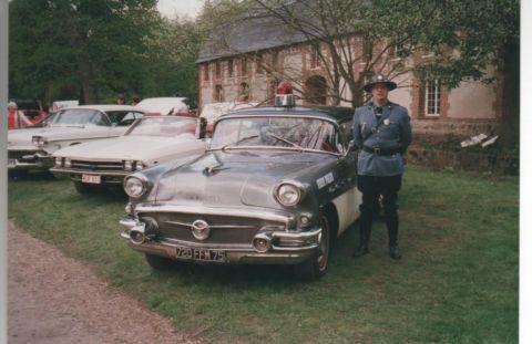 1991 Ford Crown Victoria - This 1956 Buick Century police car is parked on grass with a uniformed officer beside it.