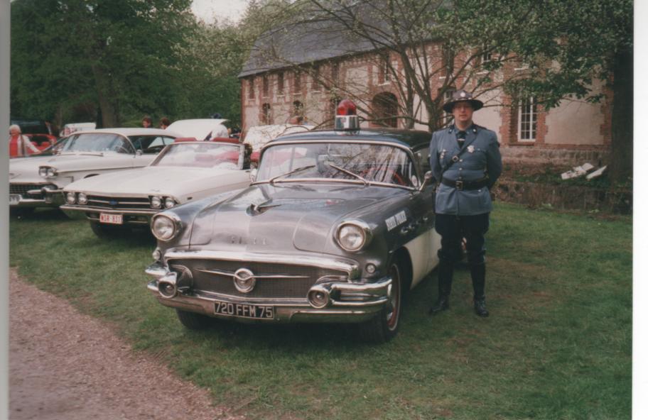 1956 Buick Century police car with officer standing next to it. Other classic cars in background