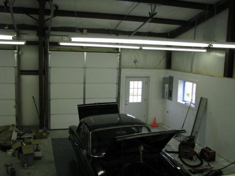 1993 Ford Bronco - A black sedan sits in a garage with its hood open, surrounded by various tools and storage items.