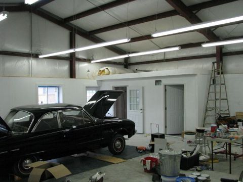 1993 Ford Bronco - A black coupe, likely from the early 1960s, sits in a workshop with its hood open, surrounded by tools and supplies.