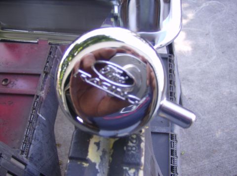 1970 Ford Ranchero - A close-up of a chrome knob a Ford Ranchero emblem, reflecting a hand and the surrounding environment.