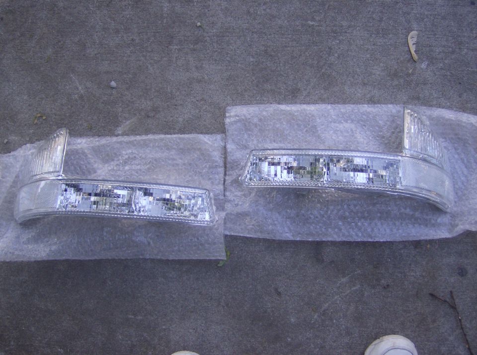 Two clear plastic marker lights on a gray concrete surface, wrapped in plastic