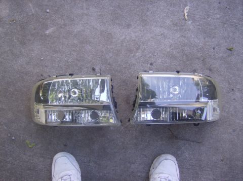 1970 Ford Ranchero - Two headlights are shown resting on a concrete surface, with a person's feet visible in the foreground.