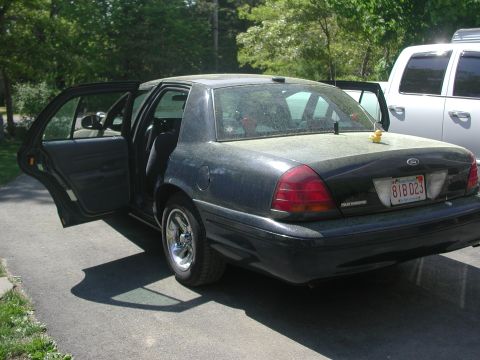 1999 Ford Crown Victoria - Rear view of a dark Ford Crown Victoria with its doors open, parked next to a white truck.