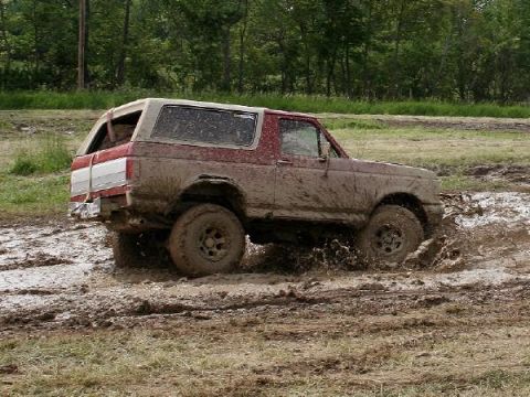 1988 Ford Bronco - This 1988 Ford Bronco is navigating a challenging muddy terrain, kicking up significant spray.