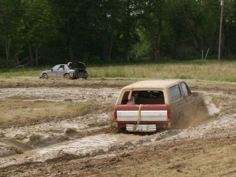 1988 Ford Bronco - A Ford Bronco navigates a muddy track, while another car sits abandoned in the background.