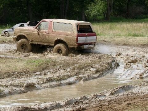 1988 Ford Bronco - A muddy SUV navigates a challenging off-road course, with another vehicle in the background.