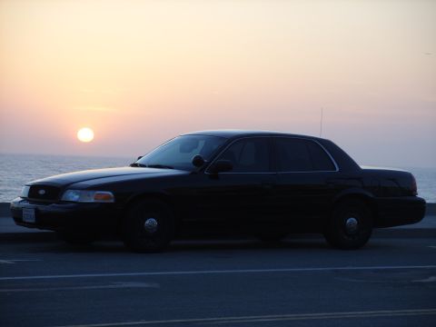 2005 Ford Crown Victoria - A black 2005 Ford Crown Victoria is parked by the ocean as the sun sets in the background.