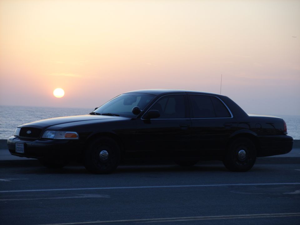 Black Ford Crown Victoria sedan in side profile against an ocean sunset