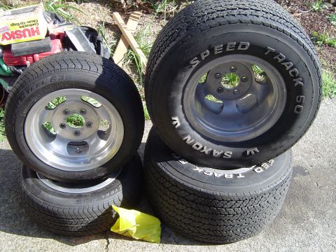 1989 Ford Bronco - A set of four tires and wheels, including two with Saxon brand rims and two with Speed Track 50 tires, are stacked outdoors.
