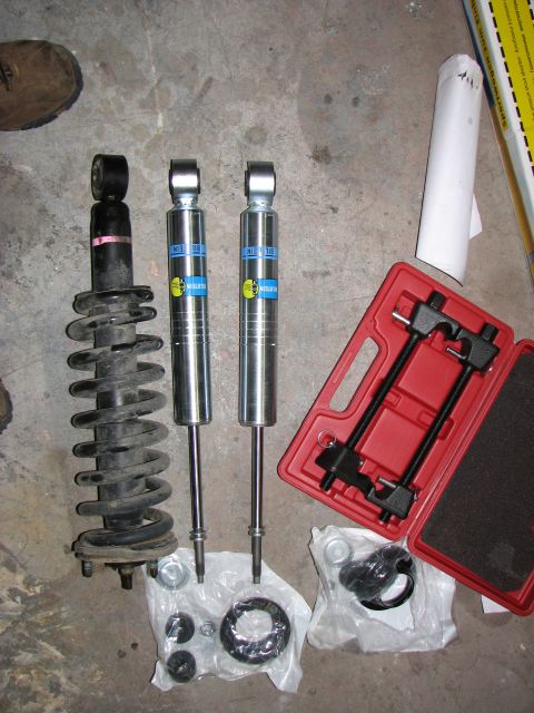 2002 Toyota Sequoia - A collection of new and old shock absorbers, along with a spring compressor tool, are laid out on a concrete floor.