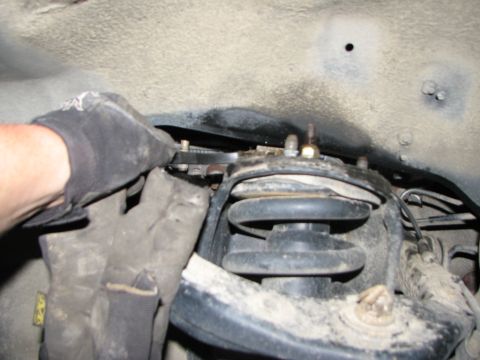 2002 Toyota Sequoia - A gloved hand uses a wrench on a suspension component. The SuperMotors.net logo is visible in the lower right corner.