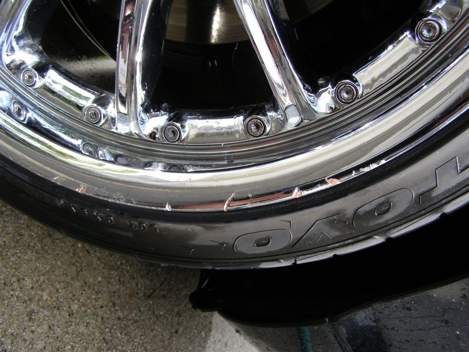 Chrome wheel with curb rash and visible tire sidewall text